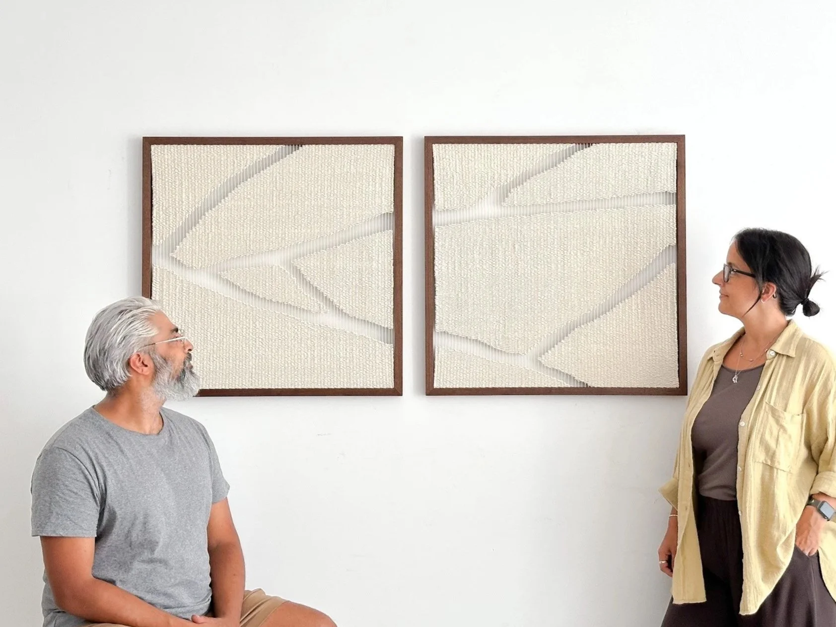 Artists Ana Salazar and Prash Vadukul standing in their studio in front of their two large, square, white textured abstract art pieces with wooden frames | Ana Salazar Atelier
