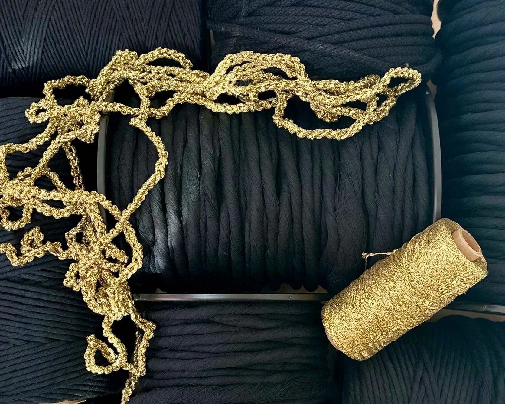 Various spools of black thread, a golden cord, and a spool of gold thread on a black surface curated for a bespoke artwork | Ana Salazar Atelier