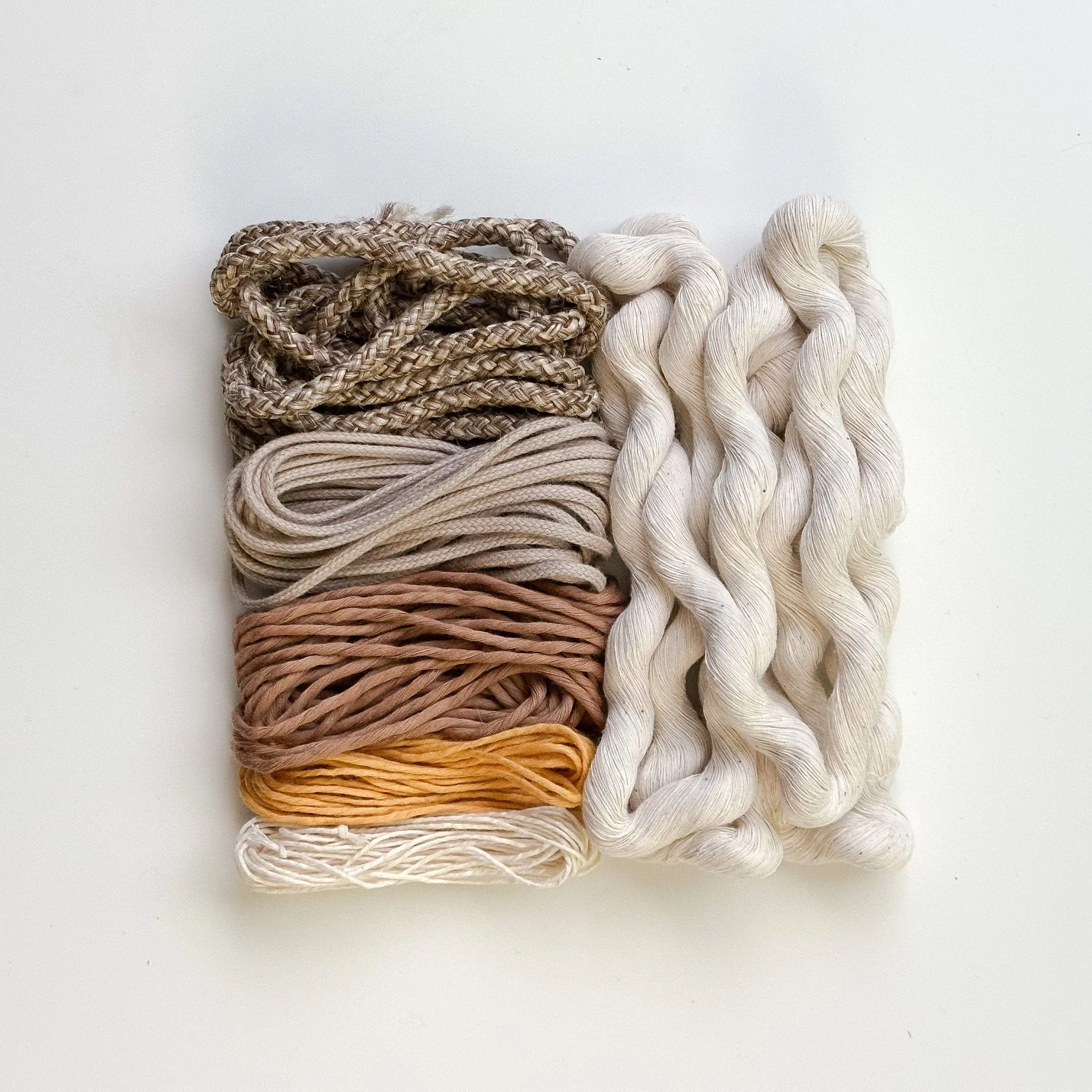 Six bundles of yarn in various colors and textures, arranged in a neat grid, with white, beige, pink, gold, gray, and a multicolored tweed yarn on white background, part of a weaving kit | Ana Salazar Atelier
