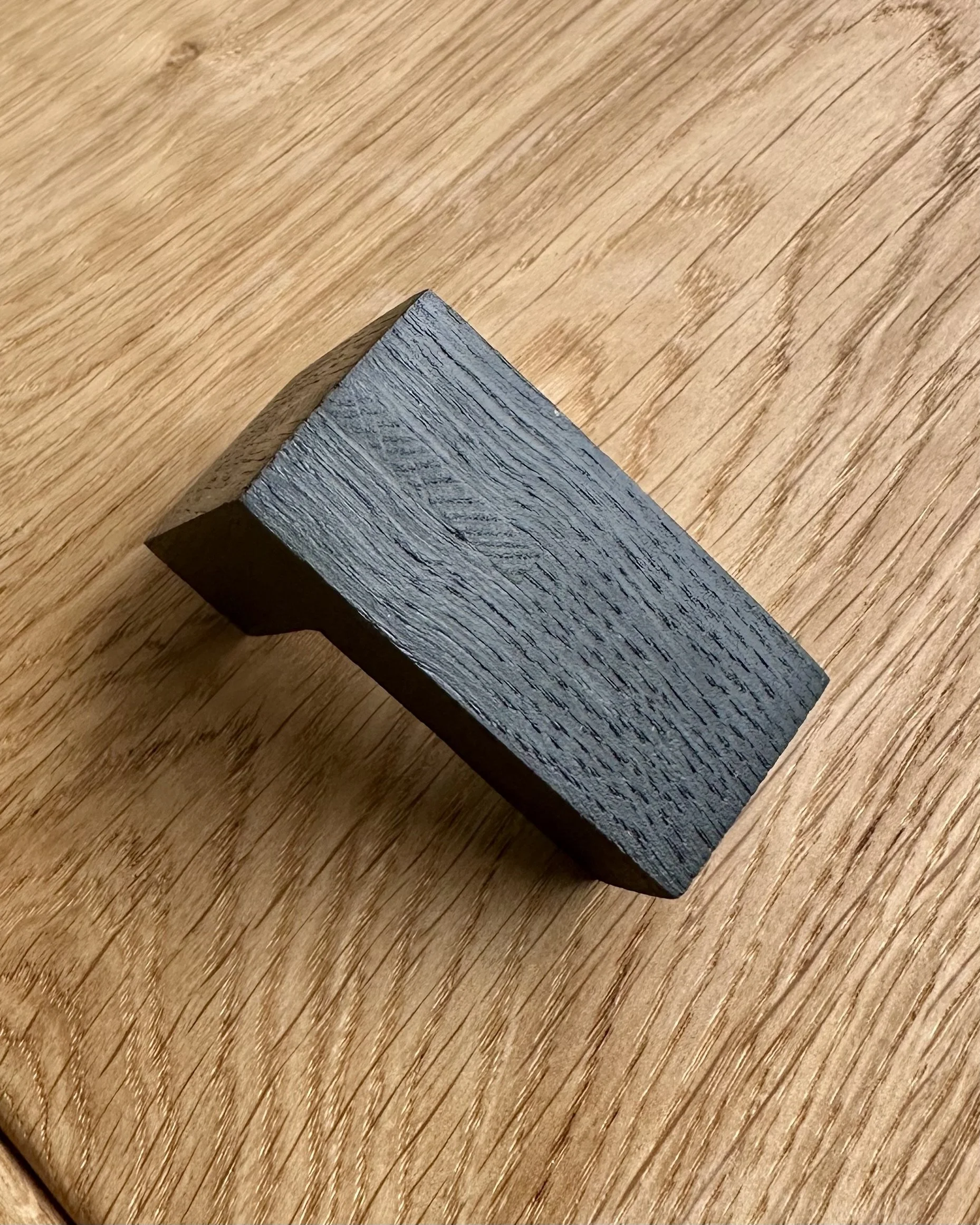 A piece of black wood with visible grain rests on a light brown wooden surface | Ana Salazar Atelier
