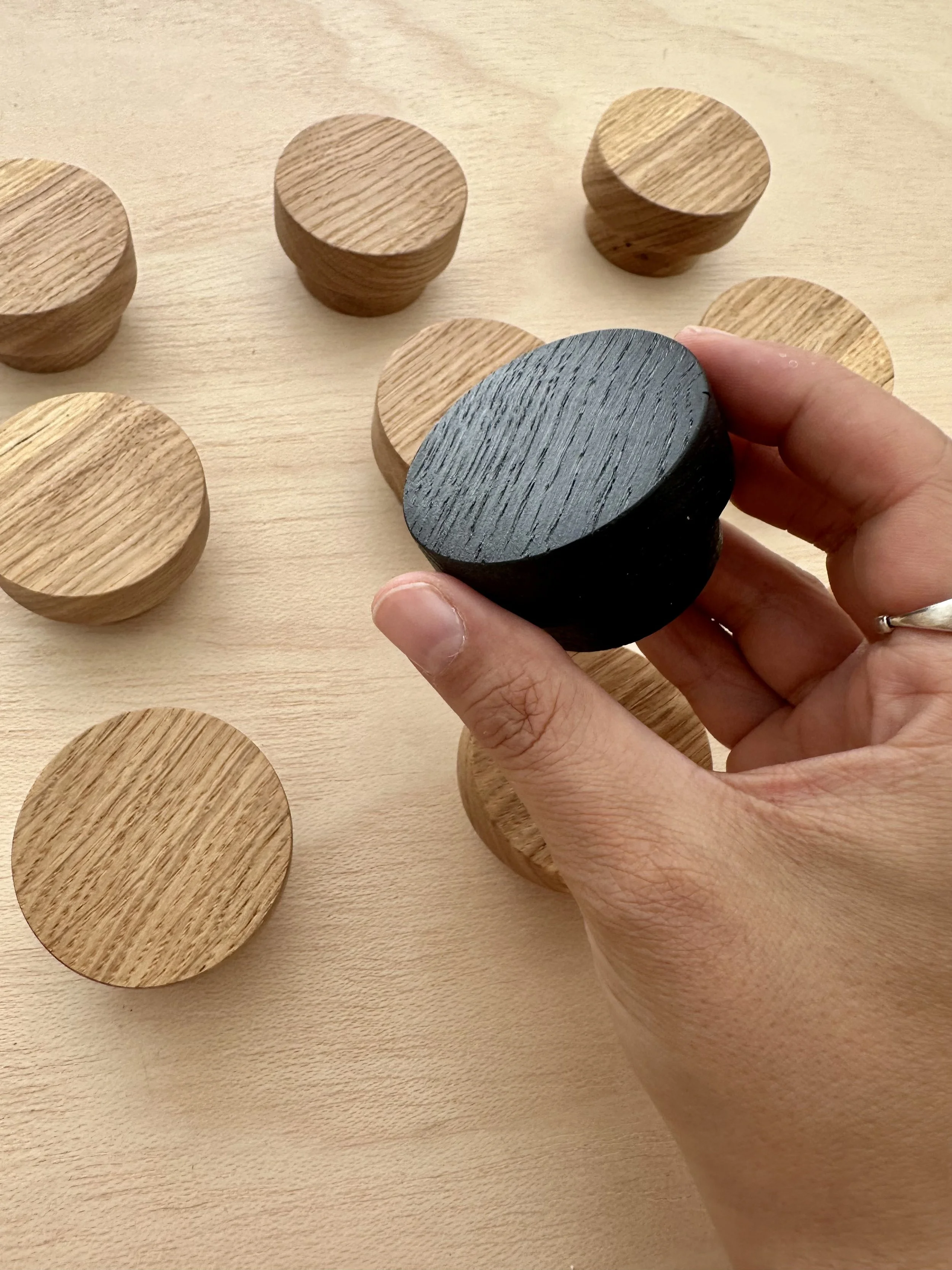 Hand holding a black wooden wall hook among several natural wooden hooks on a light wooden surface, crafted in-house by Prashant Vadukul | Ana Salazar Atelier