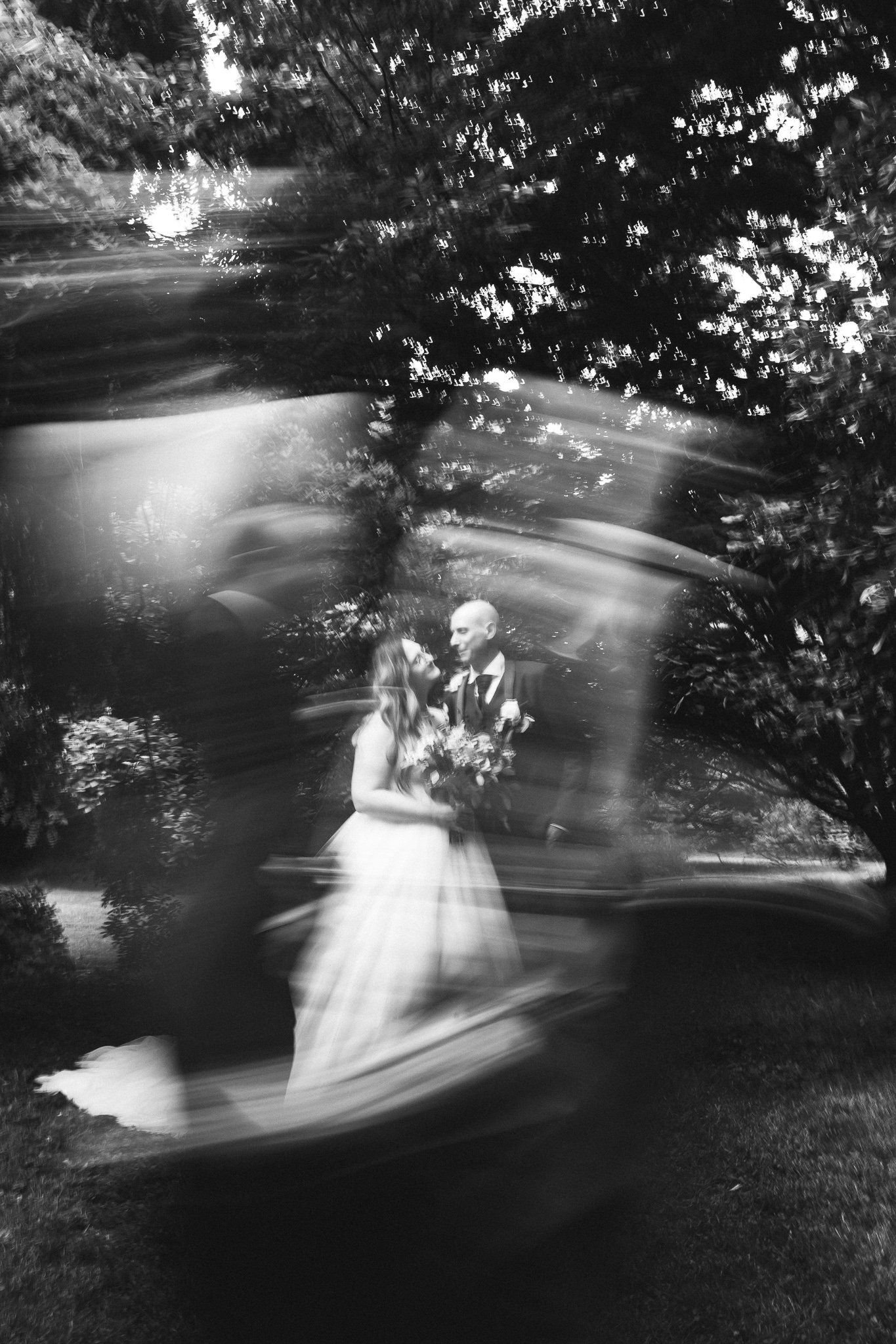 Une photographie en noir et blanc d'un couple de mariés dans un paysage naturel, prise avec un effet de mouvement ou de flou artistique.