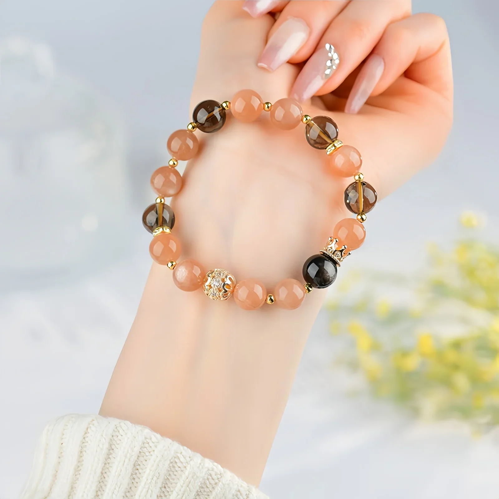 A crystal bracelet made of natural sunstone, natural black obsidian and natural smoky quartz with gold charms resting on a person's forearm
