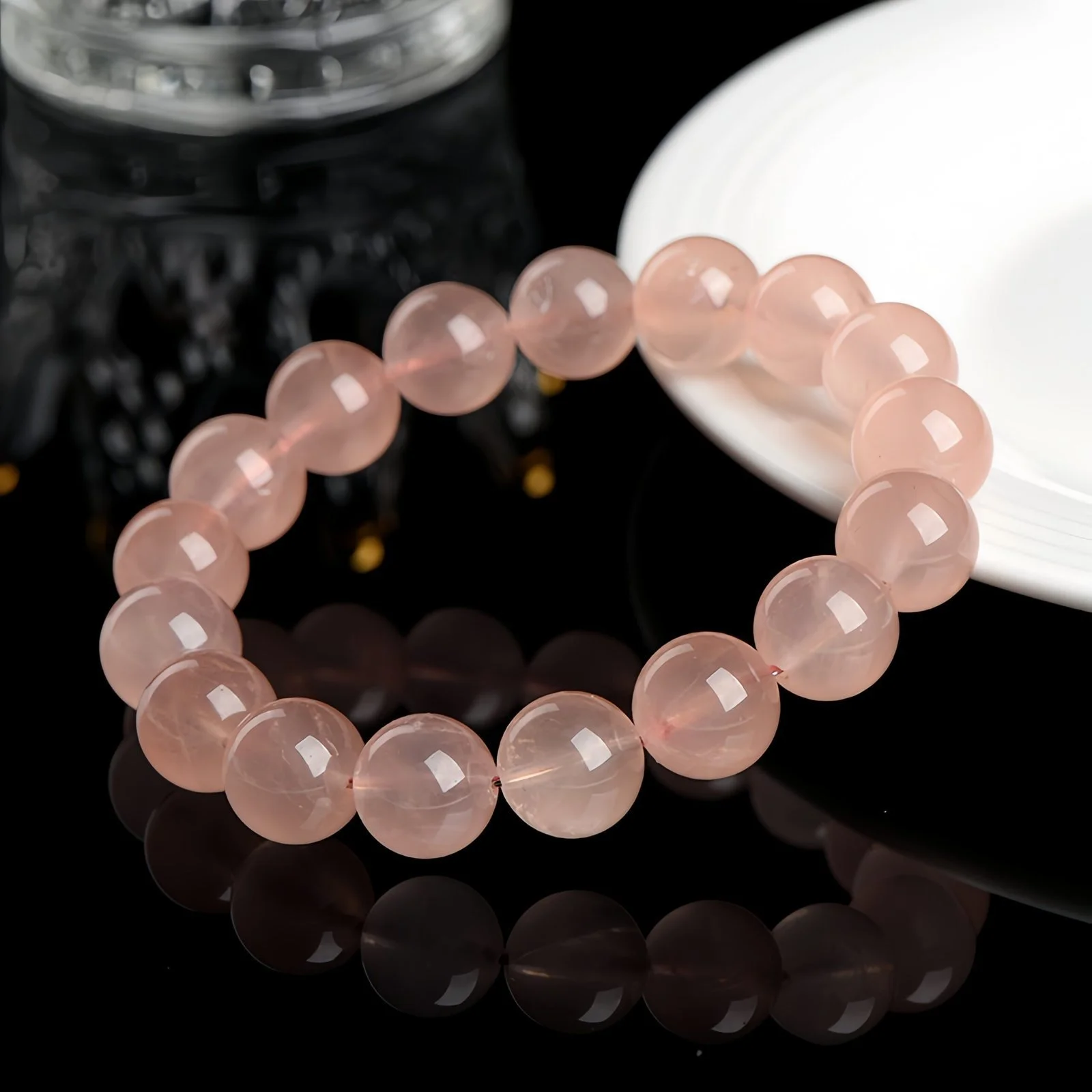 A natural Madagascan rose quartz bracelet resting on a white plate against a glossy black surface with a glass of water
