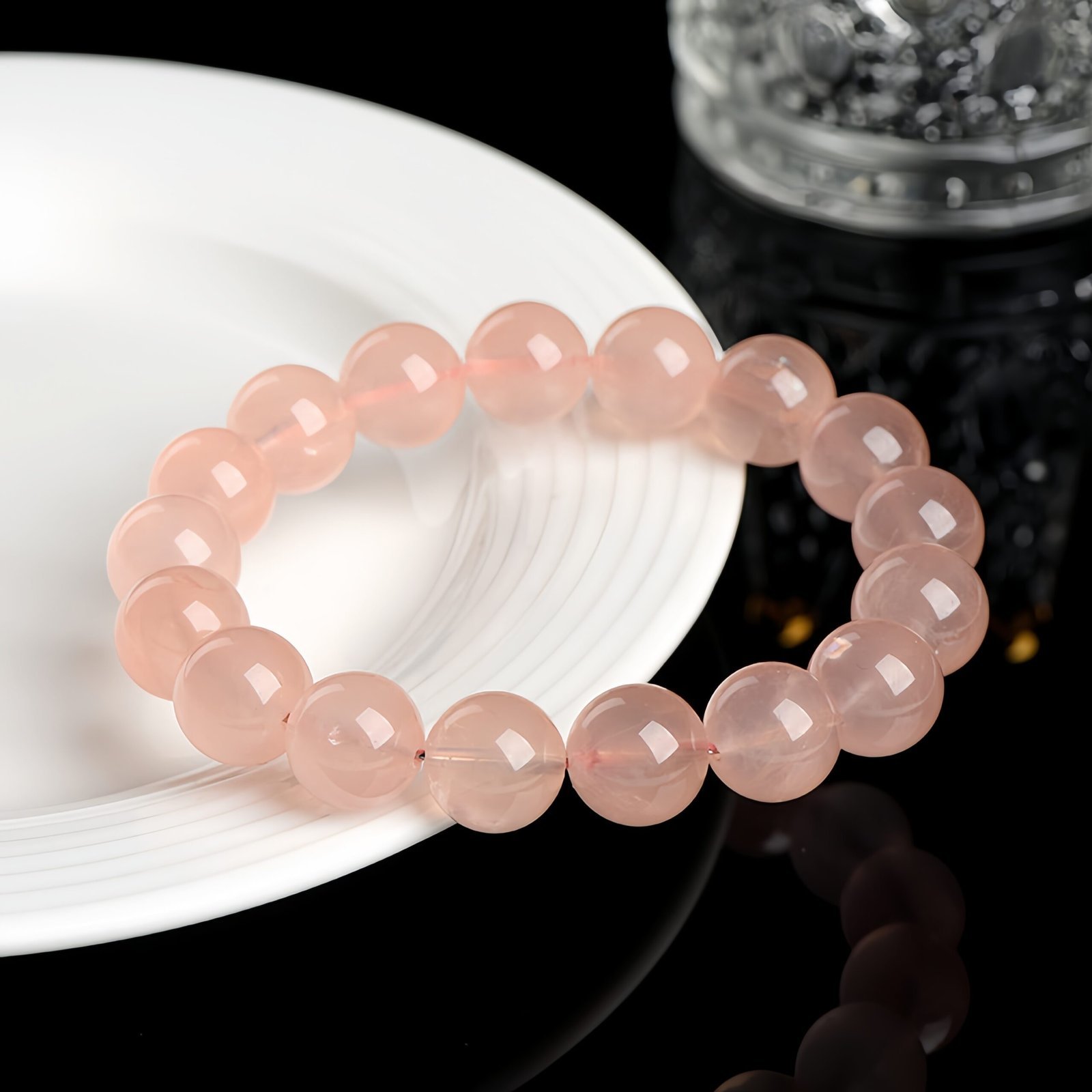A natural Madagascan rose quartz bracelet resting on a white plate against a glossy black surface with a glass of water