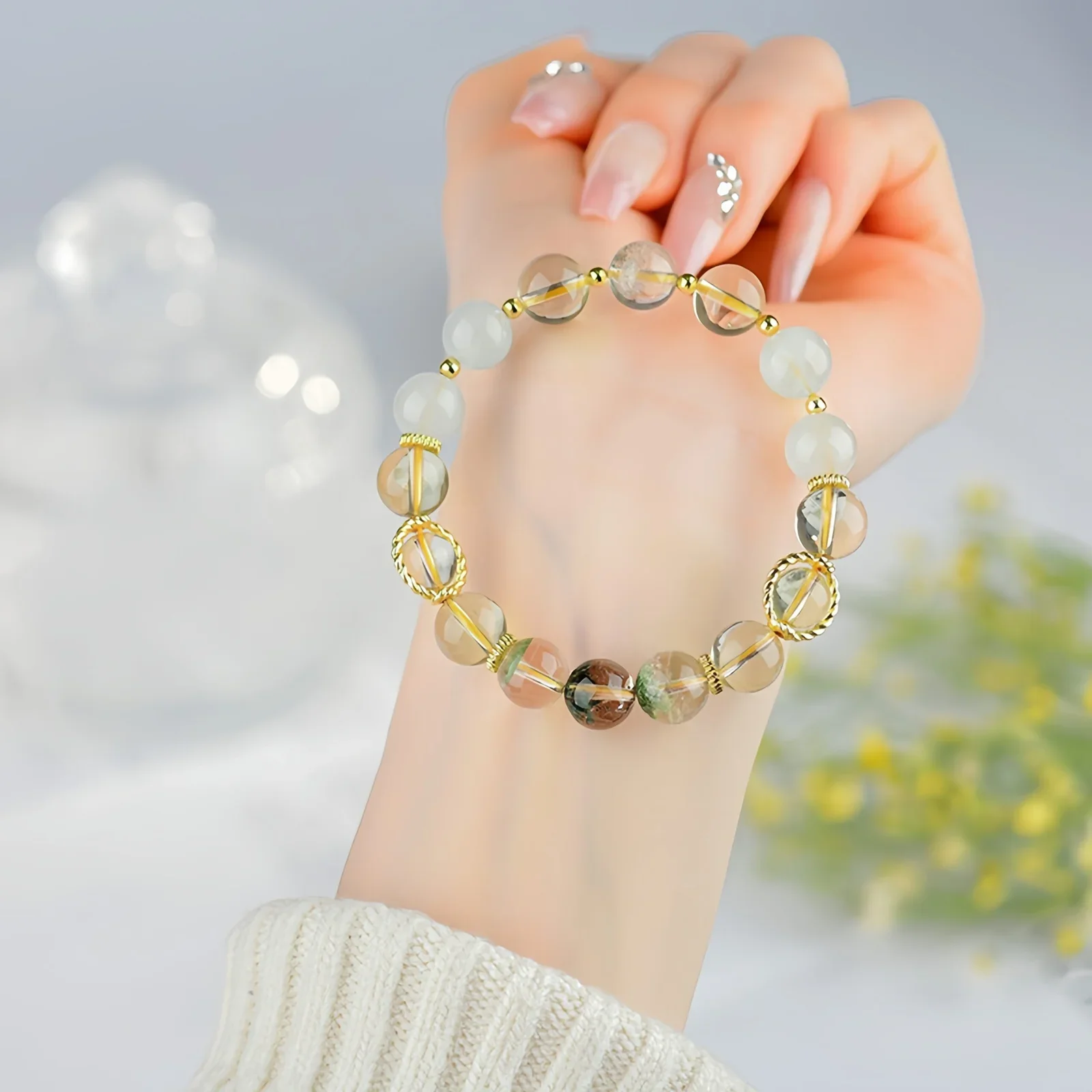 A crystal bracelet made of natural white quartz, natural green phantom quartz and natural citrine resting on a person's forearm
