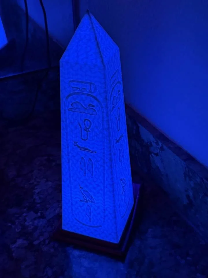 A tall, pyramid-shaped nightlight illuminated with a blue glow, featuring Egyptian hieroglyphs and symbols on its surface.