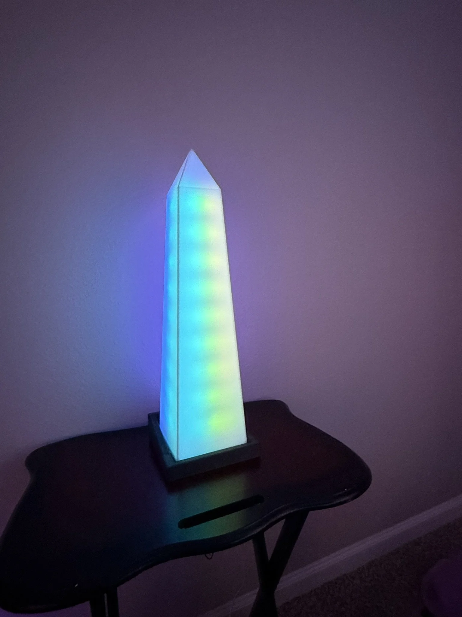 A tall, rectangular lamp with multicolored LED lights in a dark room, placed on a small table.