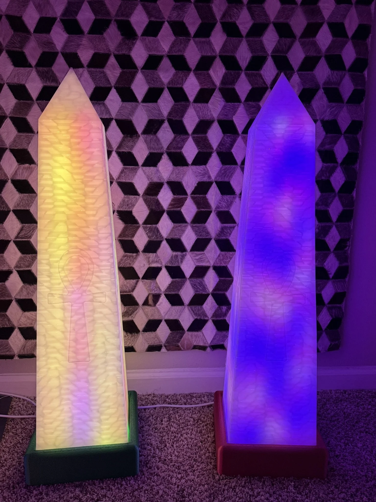 Two illuminated LED panels, one with warm yellow and pink lights and the other with cool blue lights, stand side by side on a patterned carpet with a geometric wall in the background.