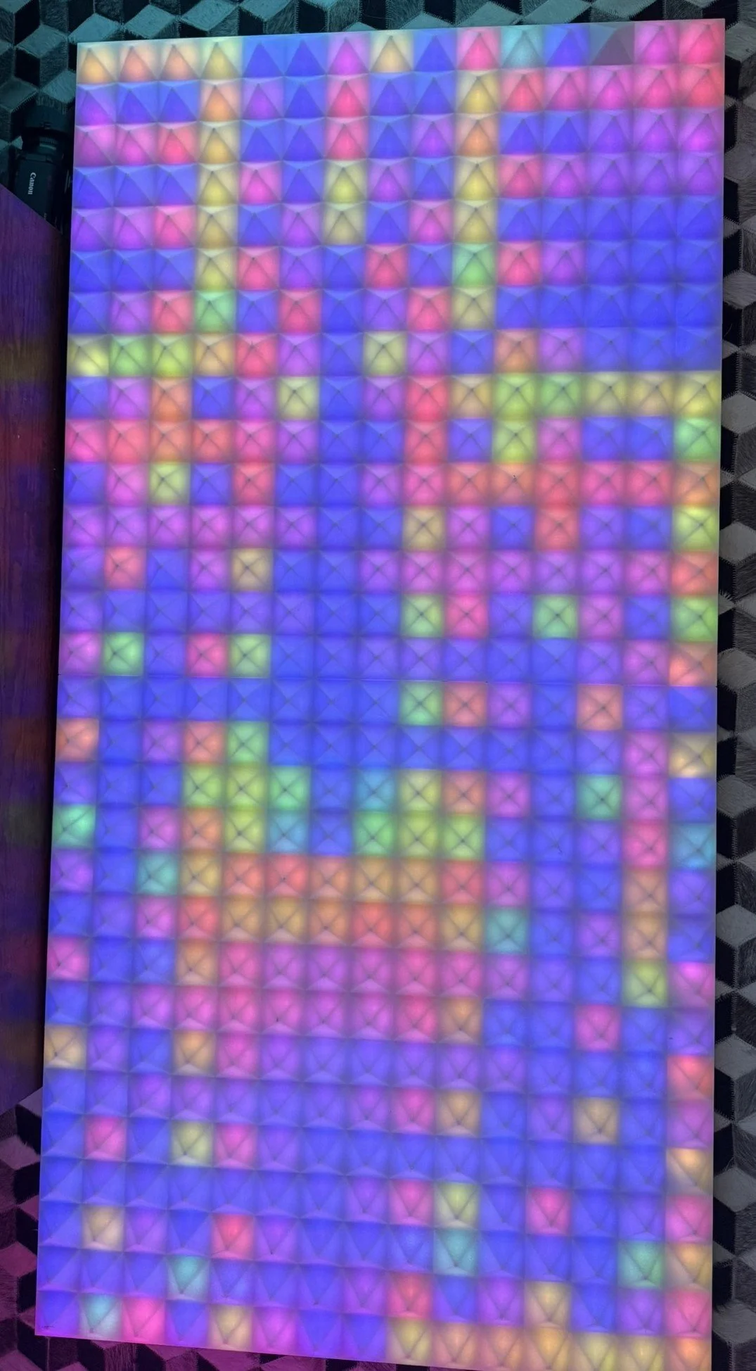 A colorful LED grid display with numerous small square lights emitting various colors, including pink, purple, blue, green, and yellow, arranged in a pattern.