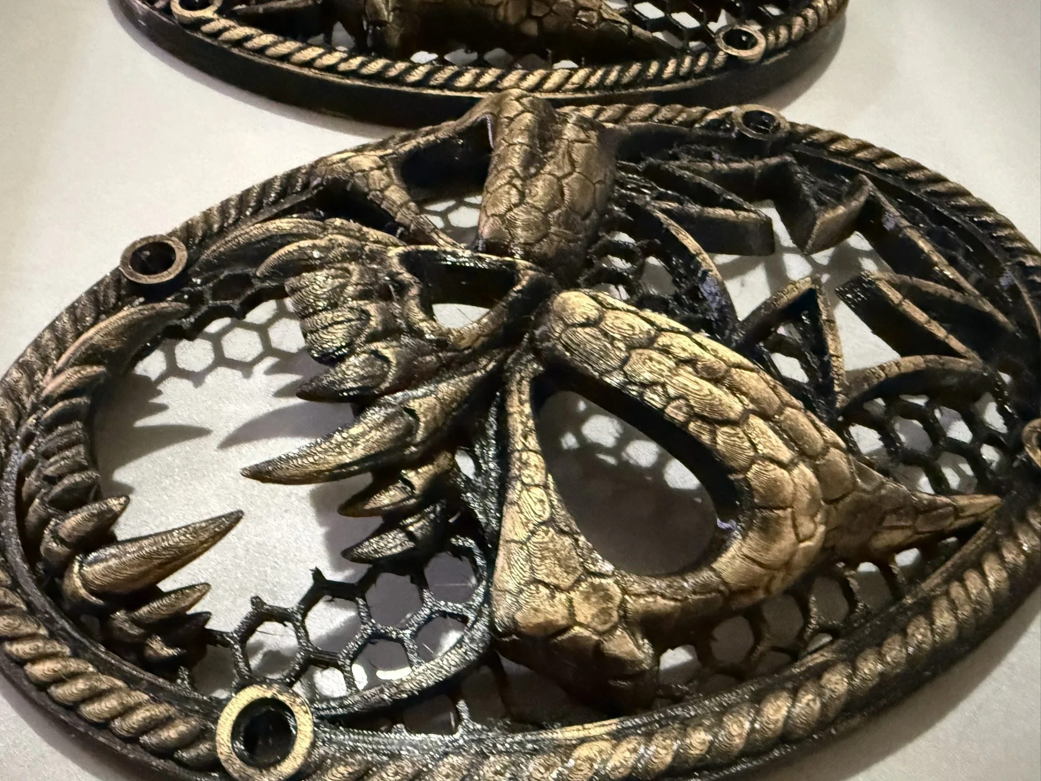 Decorative metallic scorpion-shaped piece with a netted backing and spiral embellishments, resting on a white surface.