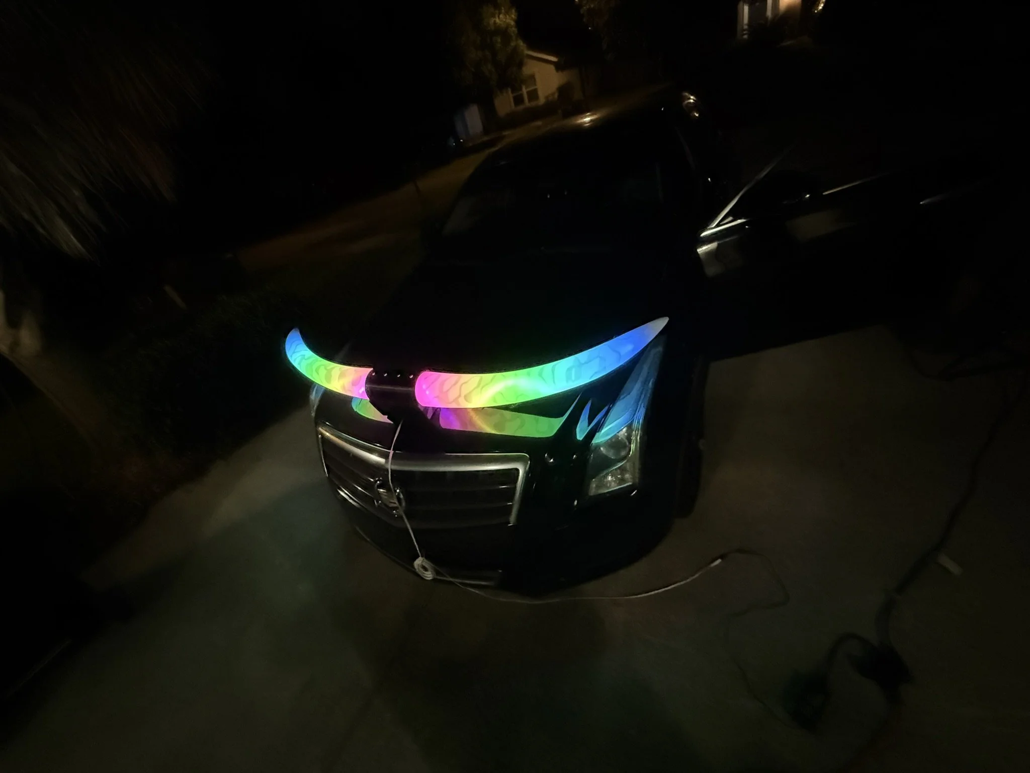 Dark image of a car with colorful rainbow LED lights on the front grille, taken at night.
