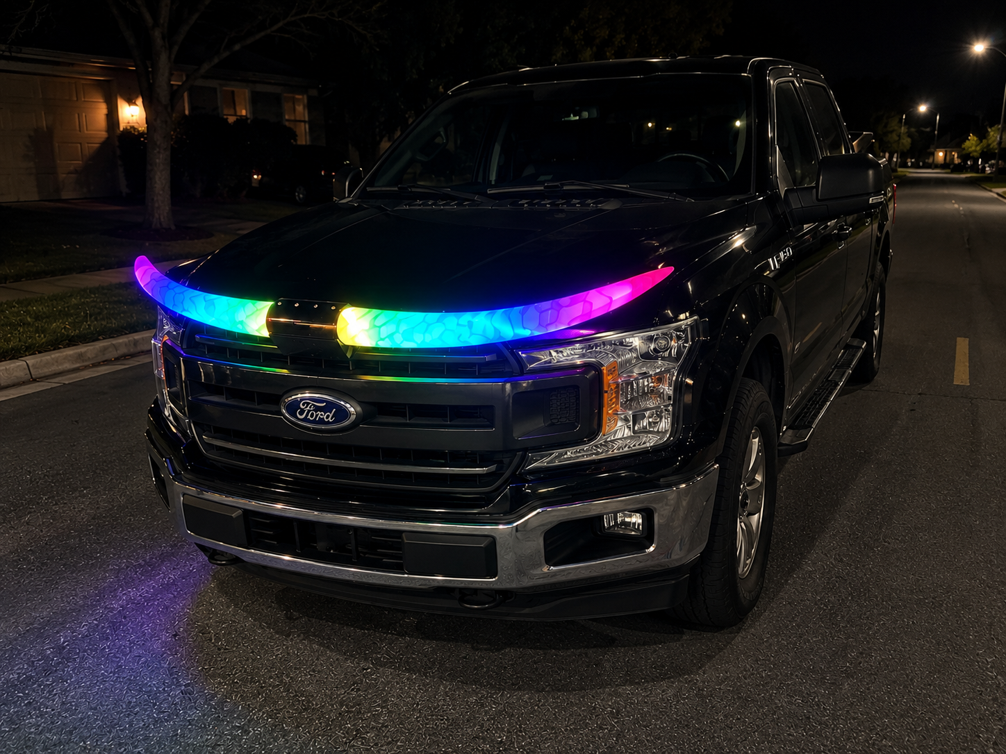 A black Ford truck parked on the street at night with colorful LED lights on the front grille.
