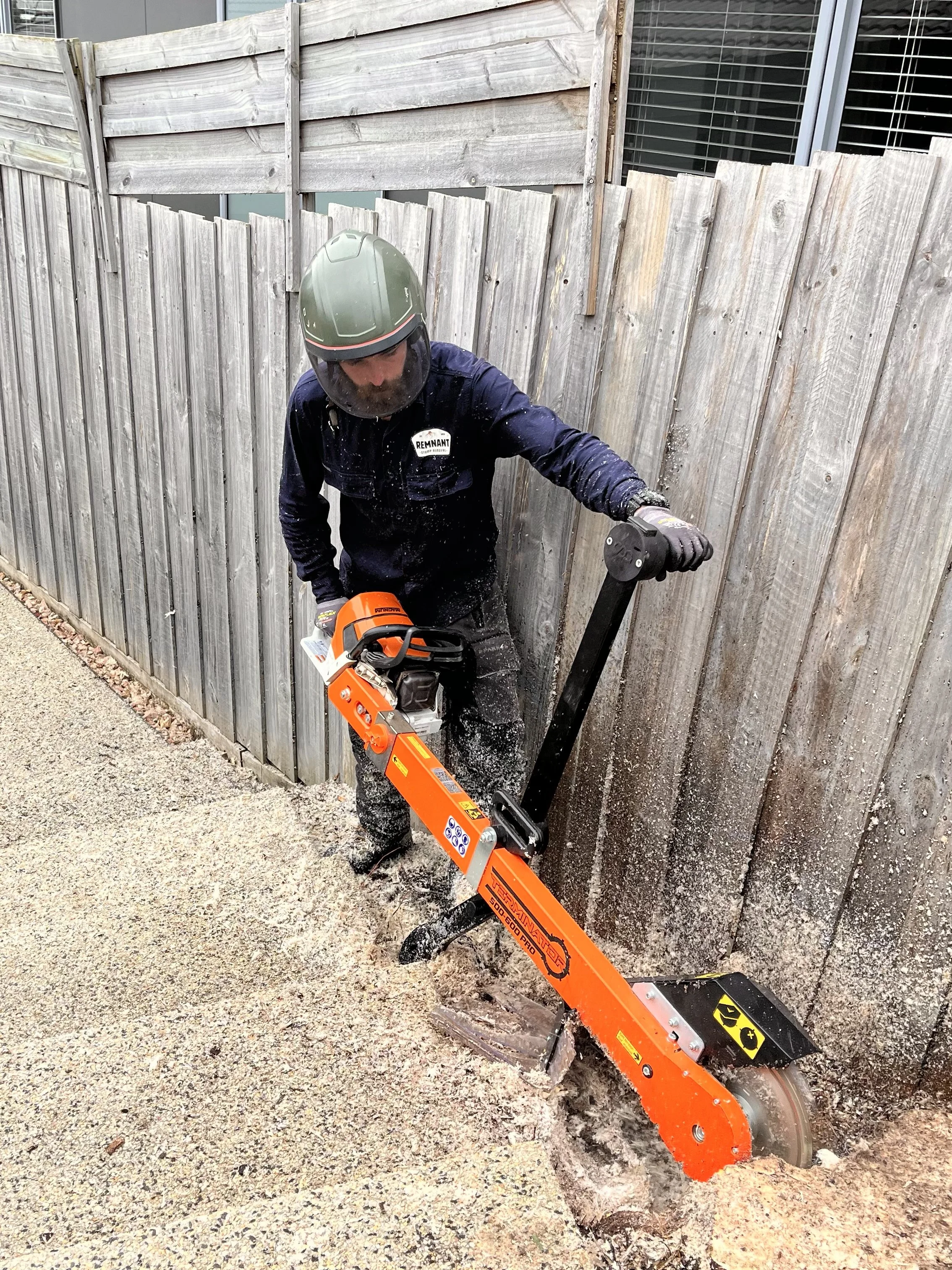 chainsaw stump grinder used to remove tight access stump in garden bed next to garden steps in backyard for landscaping, tight access machine used for below grind stump removal and grinding