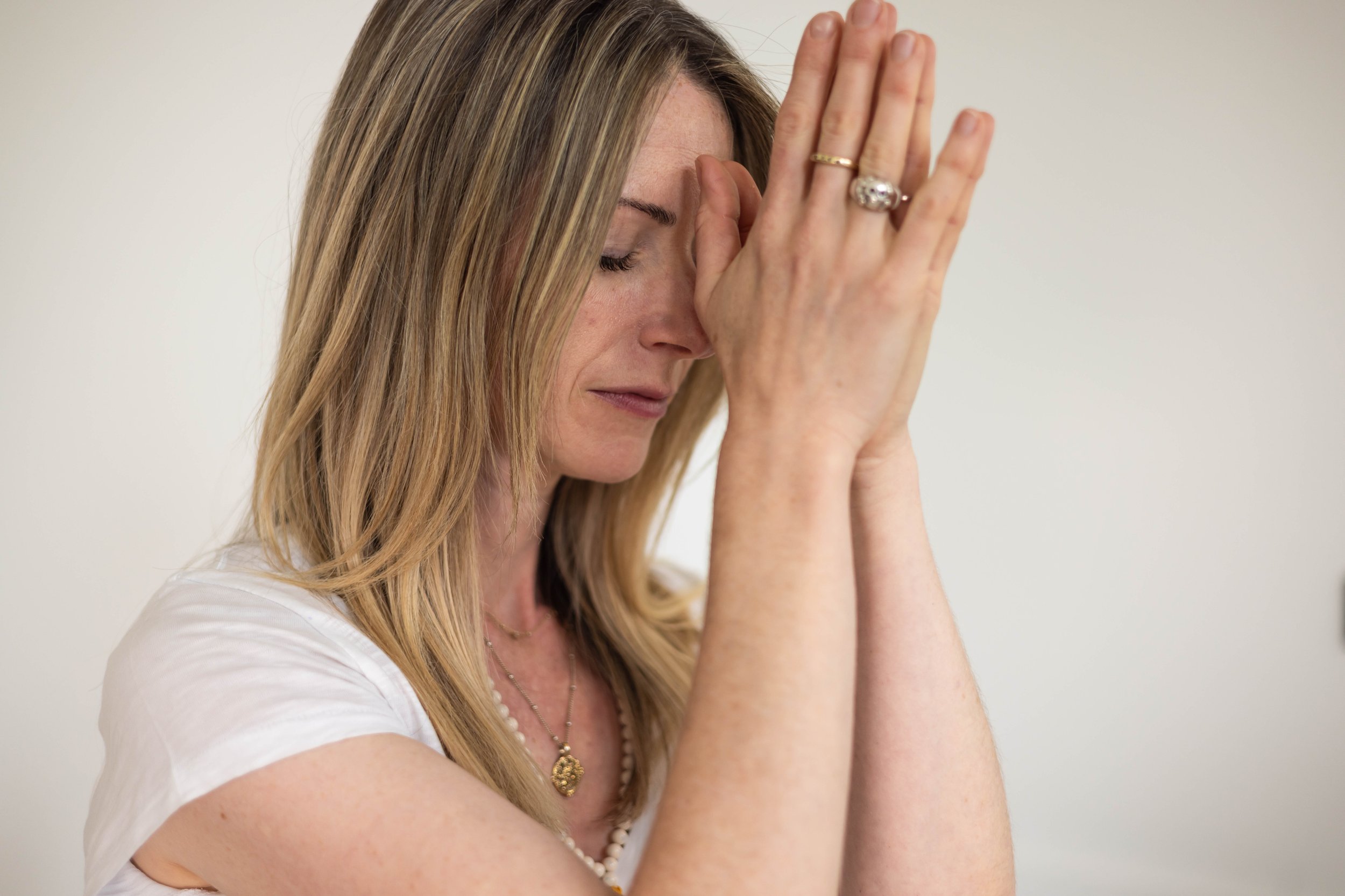 A woman with blonde hair and closed eyes praying with her hands pressed together against her forehead.