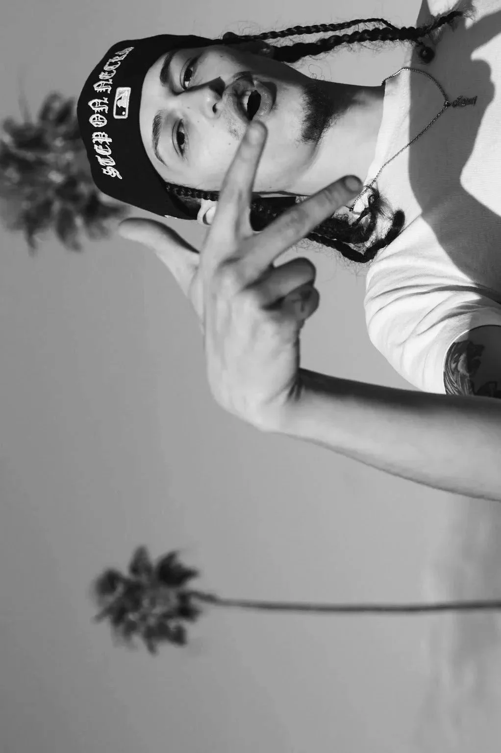 man wearing hat making peace sign with palm tree in background black and white lifestyle photography