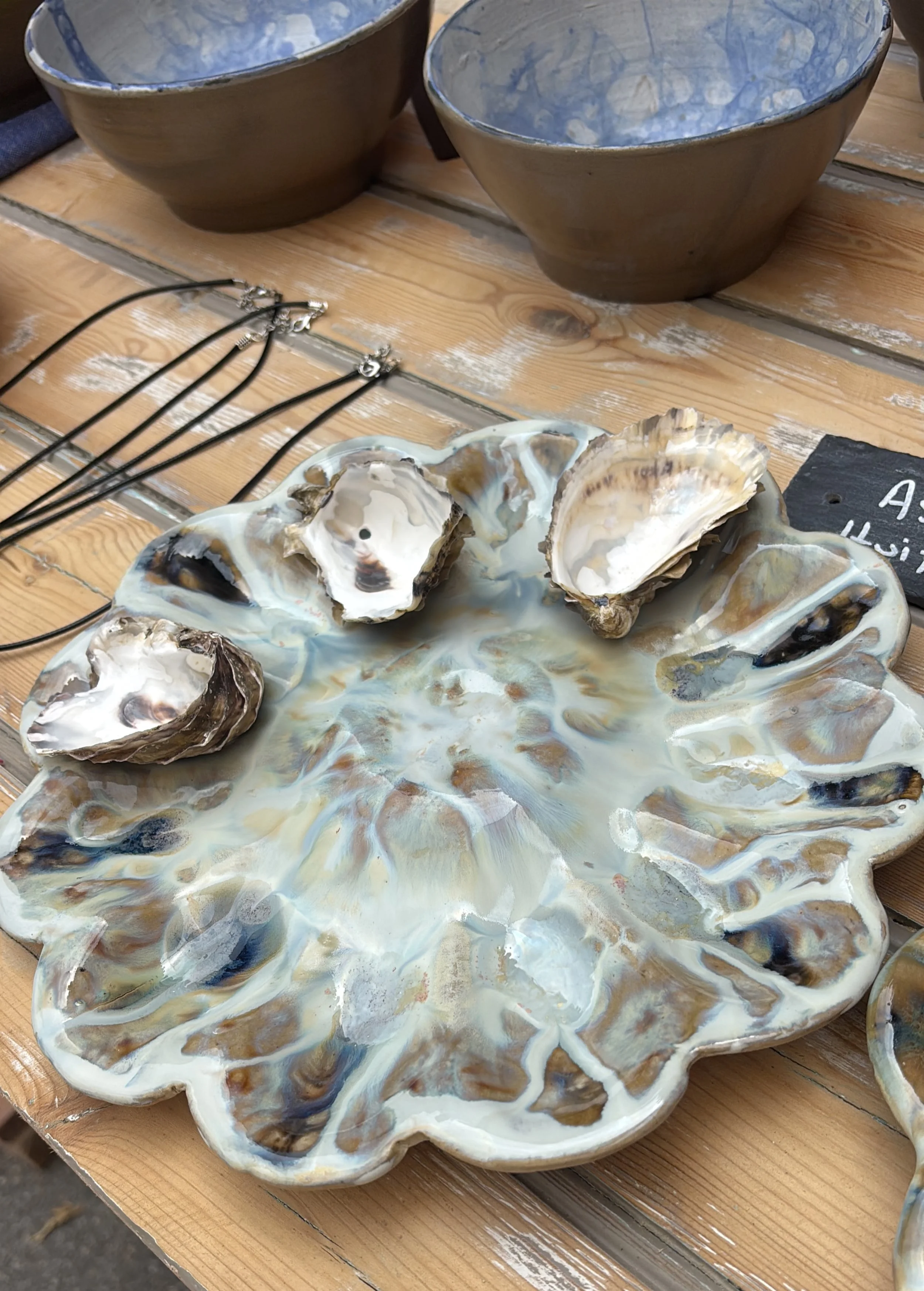 A decorative ceramic plate with open oyster shells on top, set on a wooden table with other ceramic bowls nearby.