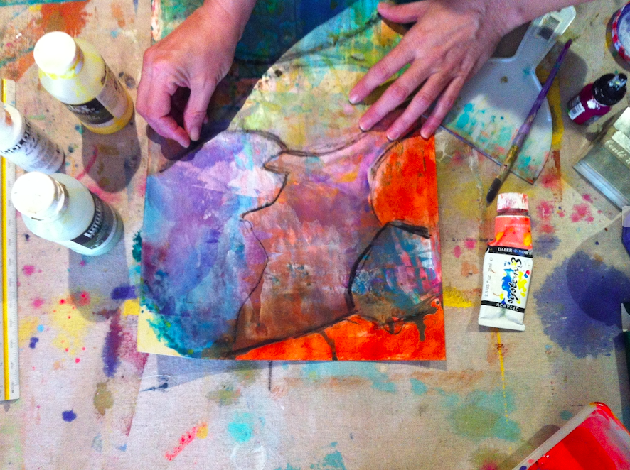 Person working on abstract watercolour painting with colours intensively blended, black outline, and various art supplies on a cluttered, colourful table.