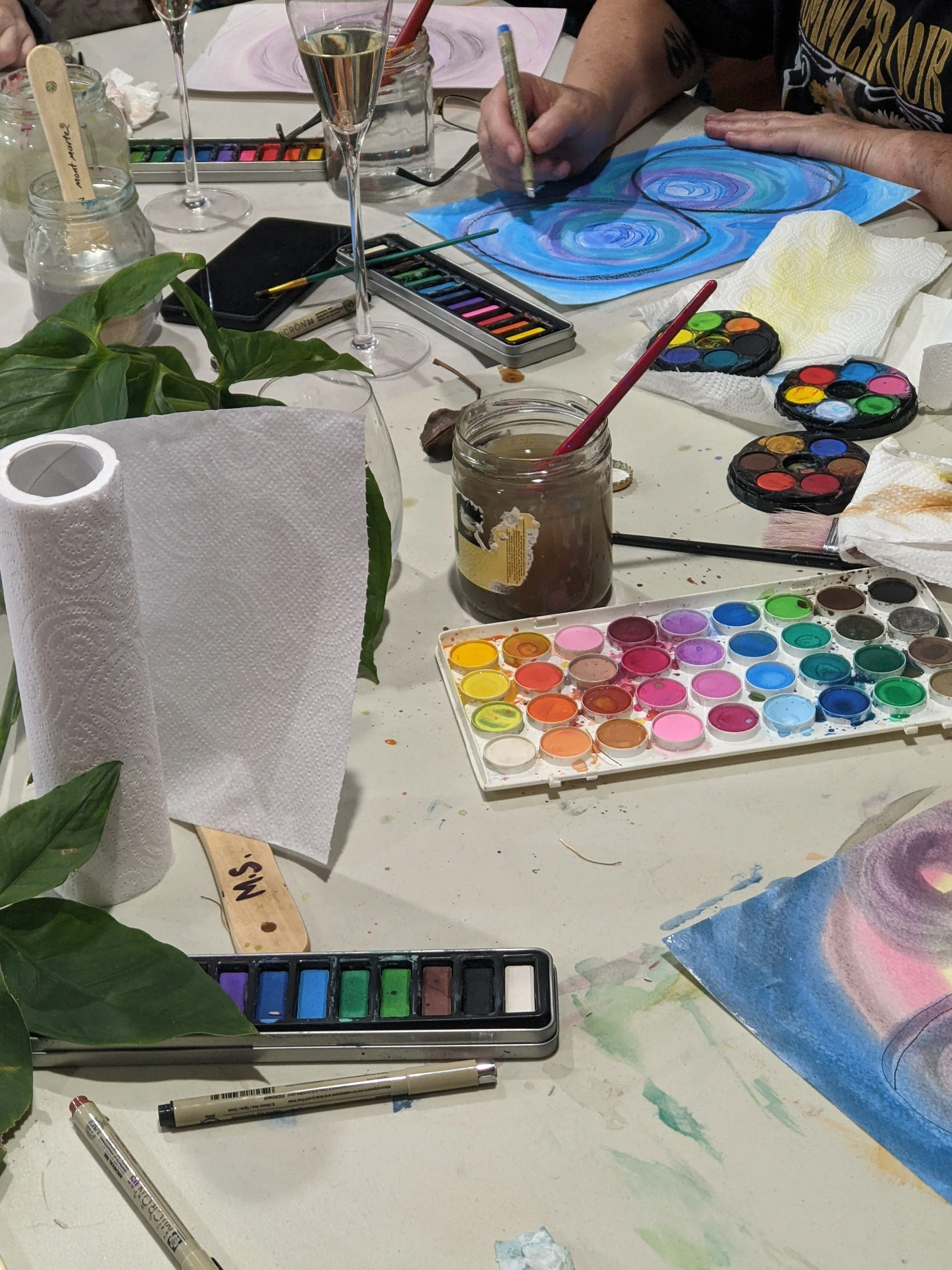 A table of art supplies and hands visible painting from a corporate art making group