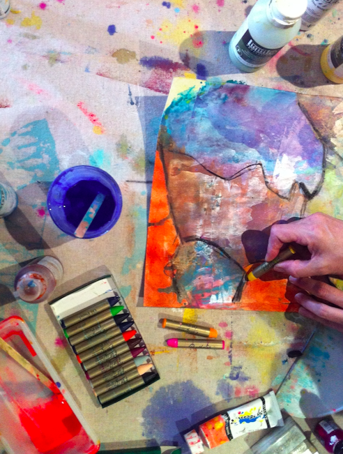 An artist's workspace with colorful paints, markers, and a person coloring or drawing on a paper with abstract art and vibrant colors.