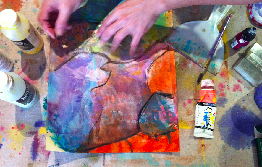 An artist creates a colourful abstract painting on paper using watercolours and ink, with supplies such as paint bottles, brushes, and a mixing palette scattered around.
