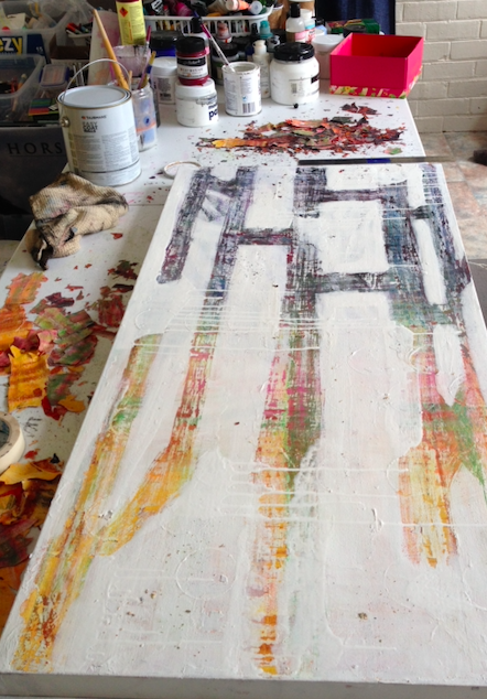 A canvas on a workspace with paint splatters and abstract design, surrounded by jars of paint, brushes, and art supplies.
