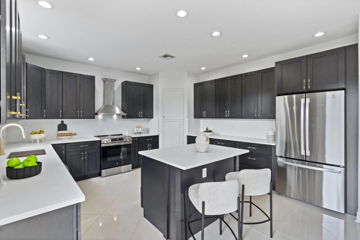 Modern kitchen with black cabinets, a white kitchen island, stainless steel appliances, white countertops, and tiled flooring.