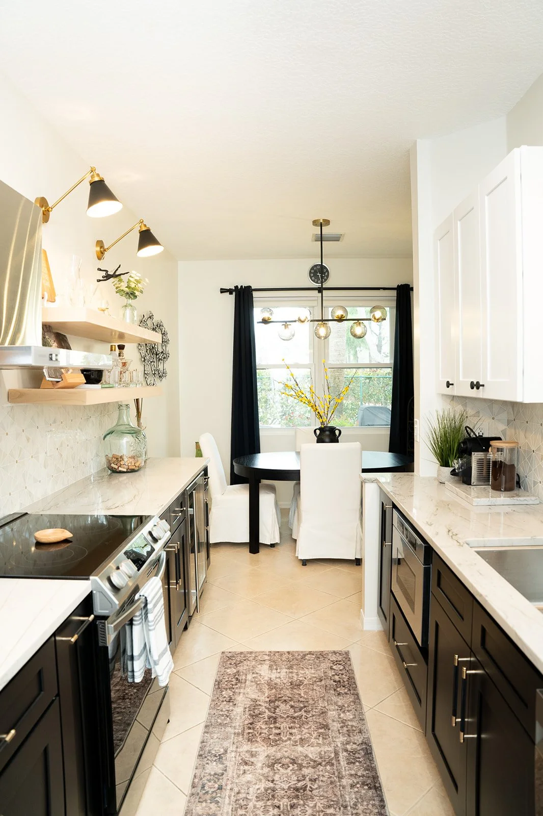 Modern kitchen with black and white cabinets, marble countertops, and a dining area with a round table and white chairs near a window with black curtains.
