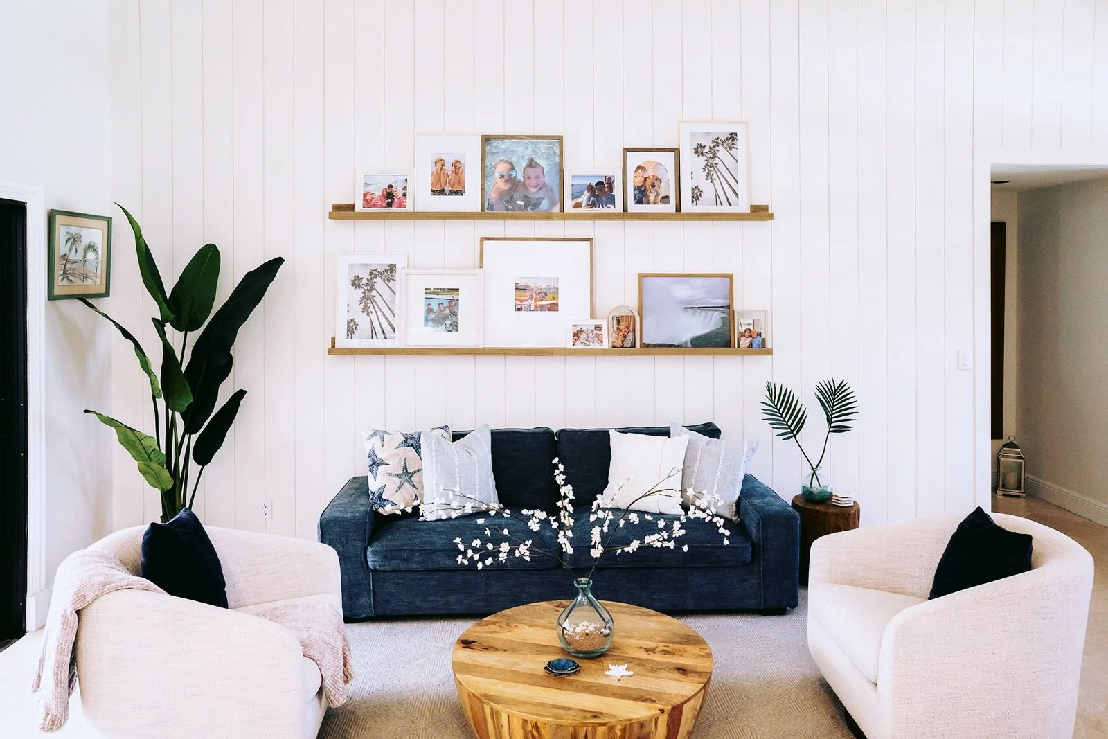 Living room with navy and white furniture, white paneled walls, and photo frames on wooden shelves.