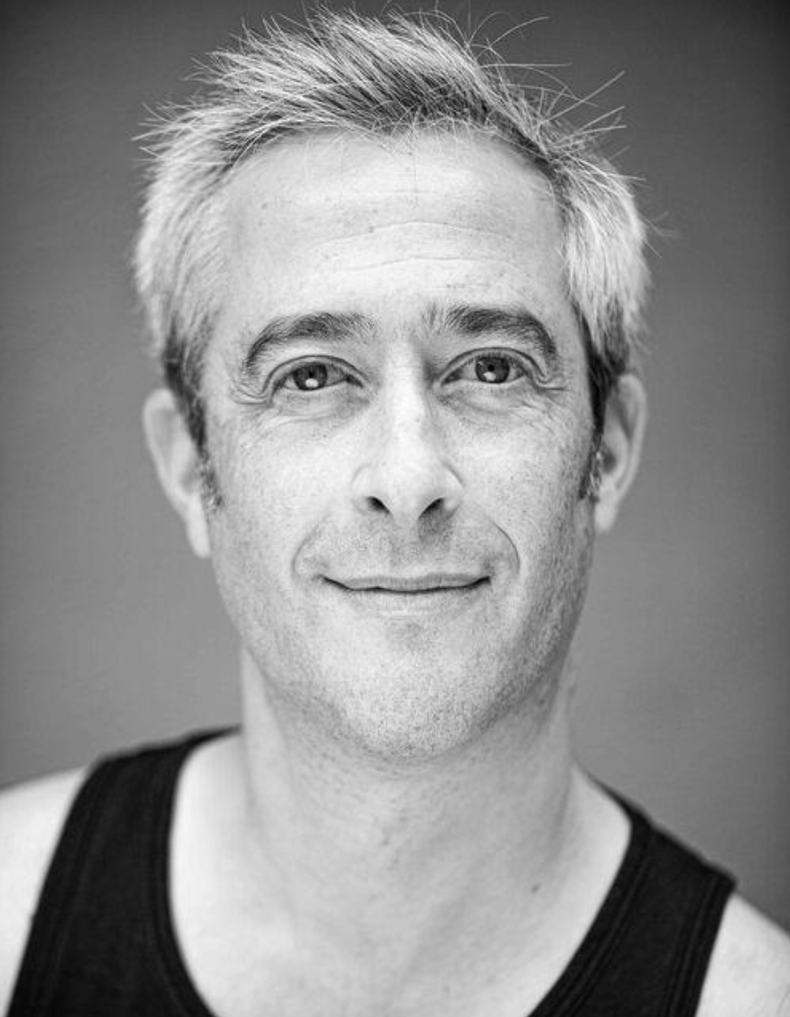 Black and white portrait of a middle-aged man with short, gray hair, smiling and wearing a sleeveless shirt.