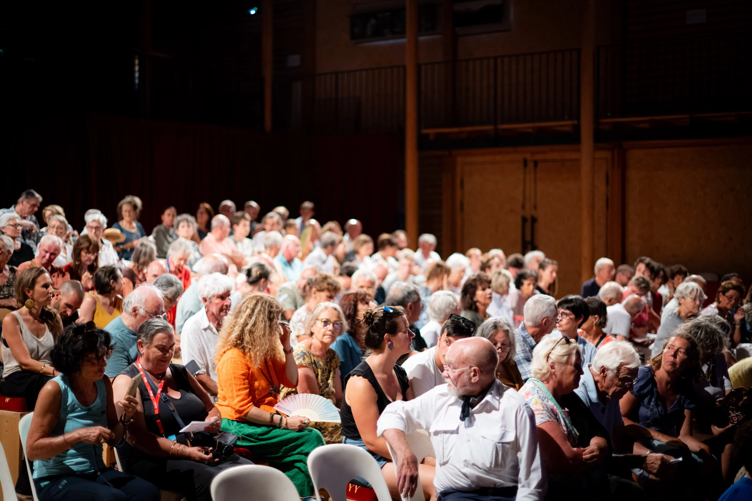 A large audience of diverse people seated in a dimly lit auditorium, facing forward, attending an event.