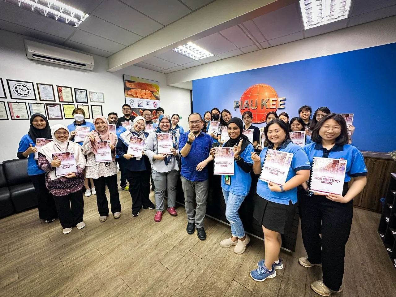 Group of people in a corporate office holding certificates for Halal Competency Training, smiling, posing for a group photo.