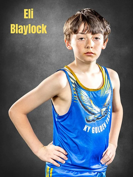 Young boy in a blue and yellow athletic uniform with a phoenix graphic and the words 'KY GOLDEN EAGLES', standing with one hand on his hip against a dark gray background. Text on the image reads 'Eli Blaylock'.