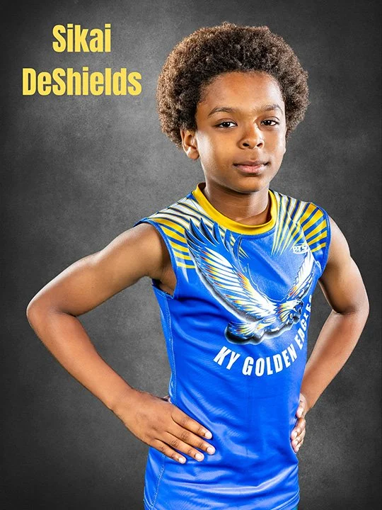 A young boy in a blue and yellow sports jersey with a winged logo and the words "KY Golden Eagle" printed on it, standing with hands on hips against a gray background, with yellow text reading "Sikai DeShields" in the top left corner.