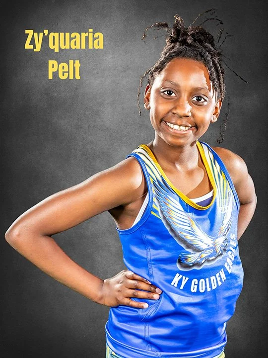 Young girl smiling, wearing a blue and yellow sports jersey with an eagle and text that reads "My Golden Eagles," against a dark background with yellow text that says "Zy'quaria Pelt."