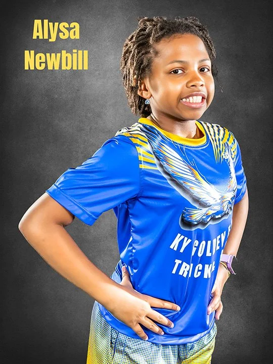 Young girl with a confident smile wearing a blue volleyball jersey with a white eagle graphic and yellow accents, standing against a dark background. Name "Alysa Newbill" is written in yellow text in the top left corner.