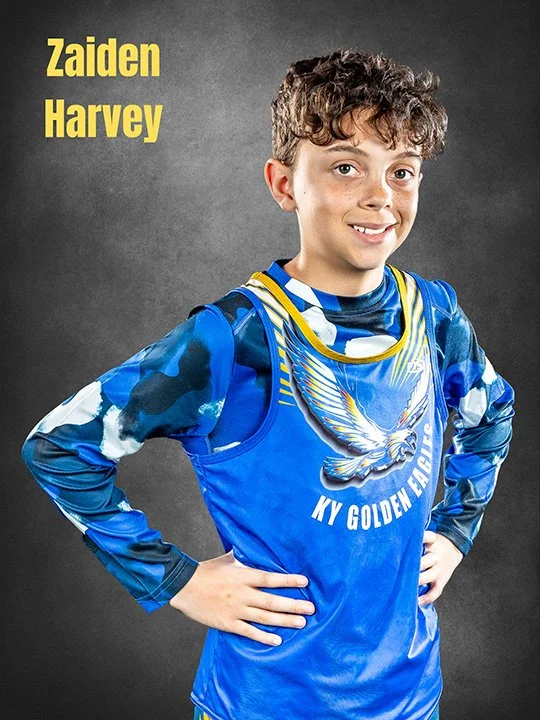 A young boy wearing a blue sports jersey with a bird logo and the words "KY Golden Eagles," standing with hands on hips against a gray background, with yellow text reading "Zaiden Harvey" in the top left corner.