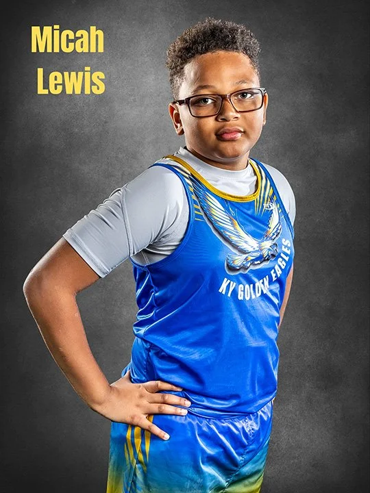 A young boy wearing glasses and a blue basketball jersey with yellow details, posed confidently with one hand on his hip against a gray background. The jersey has an eagle graphic and the words "KY GOLDEN EAGLES." The top left corner has text that re