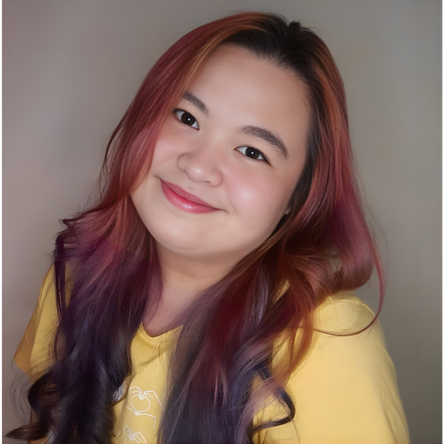 A young woman with multicolored hair and a yellow shirt, smiling at the camera.