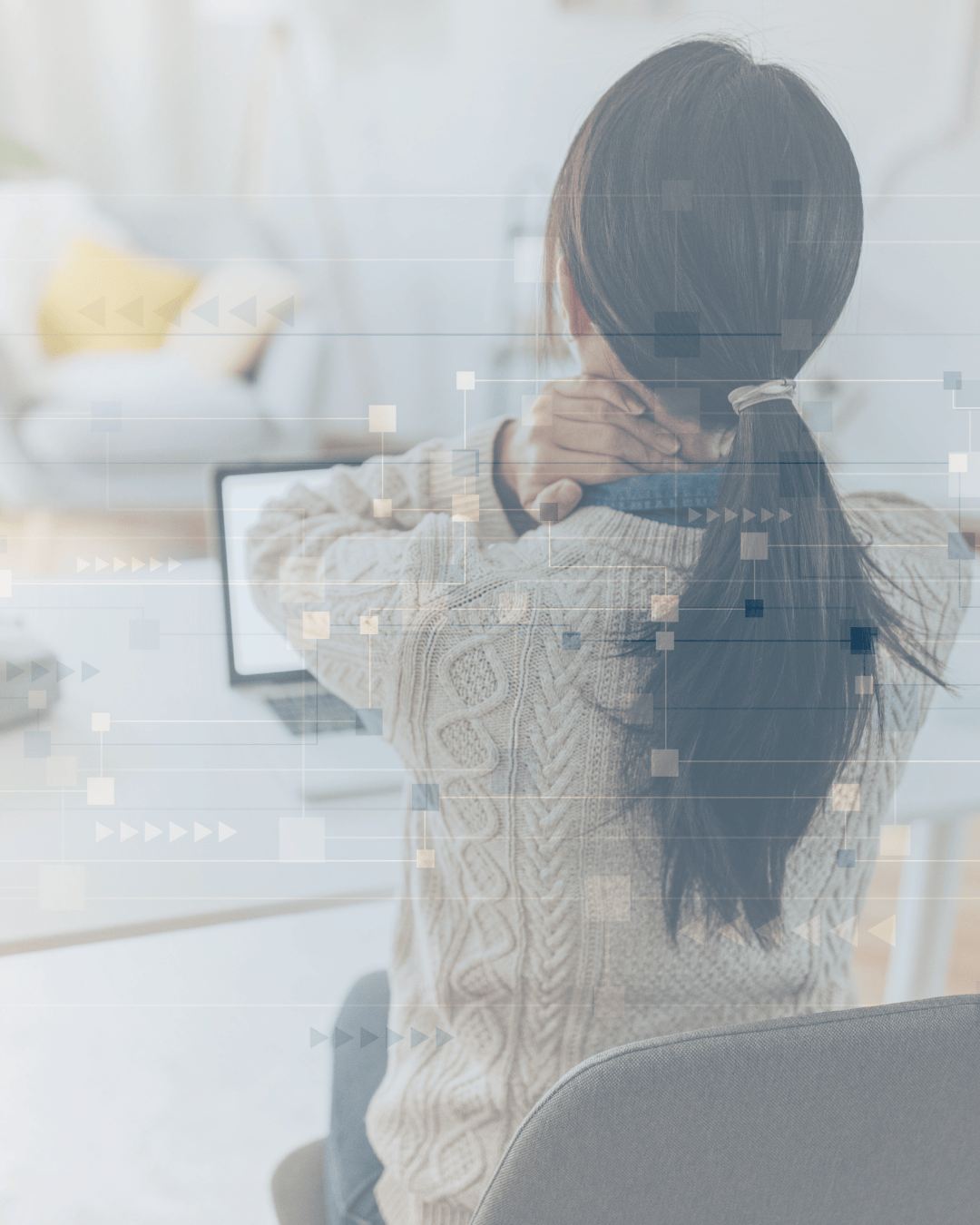 A woman with long dark hair tied in a ponytail, wearing a beige knit sweater, is sitting at a desk holding her neck with both hands, in front of a computer.