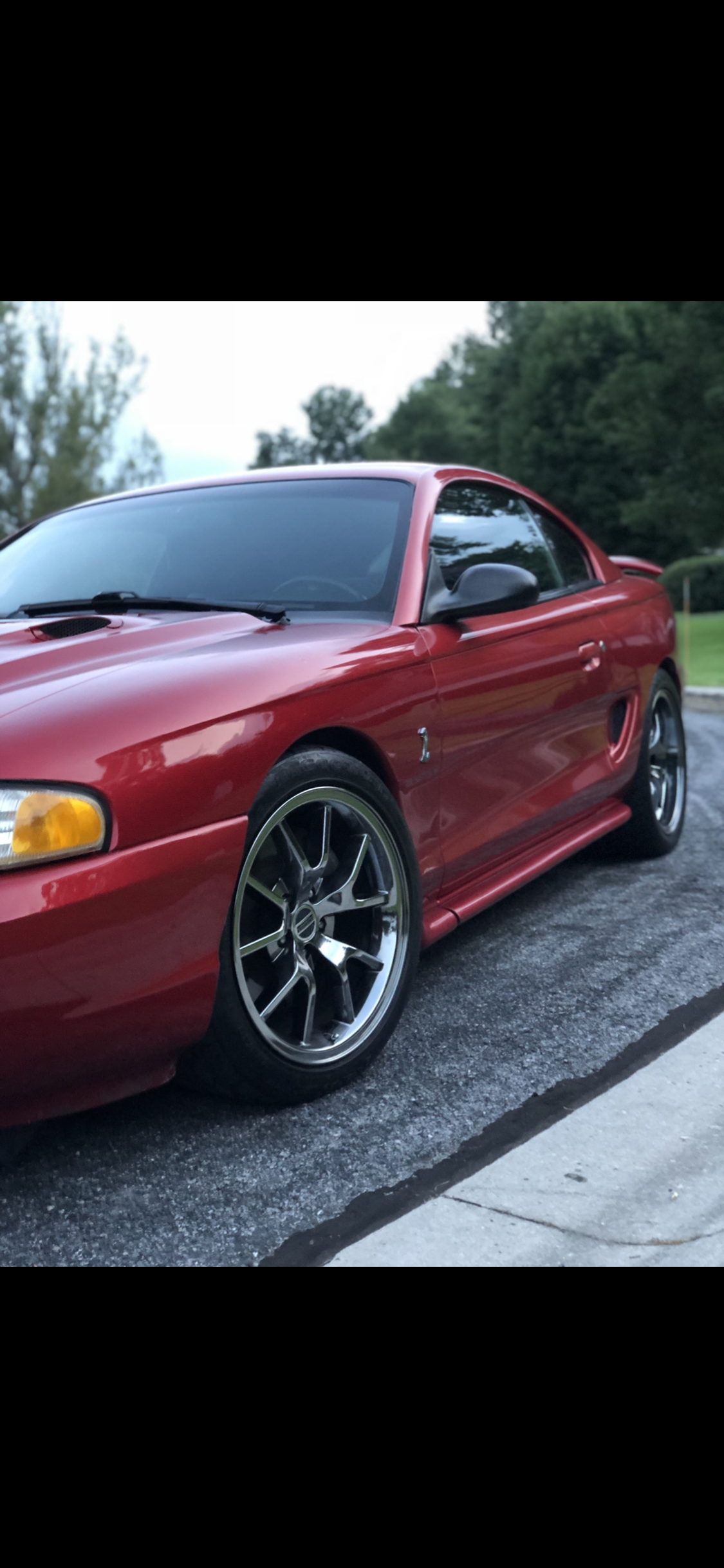 Red sporty coupe car parked on a paved surface with trees in the background.