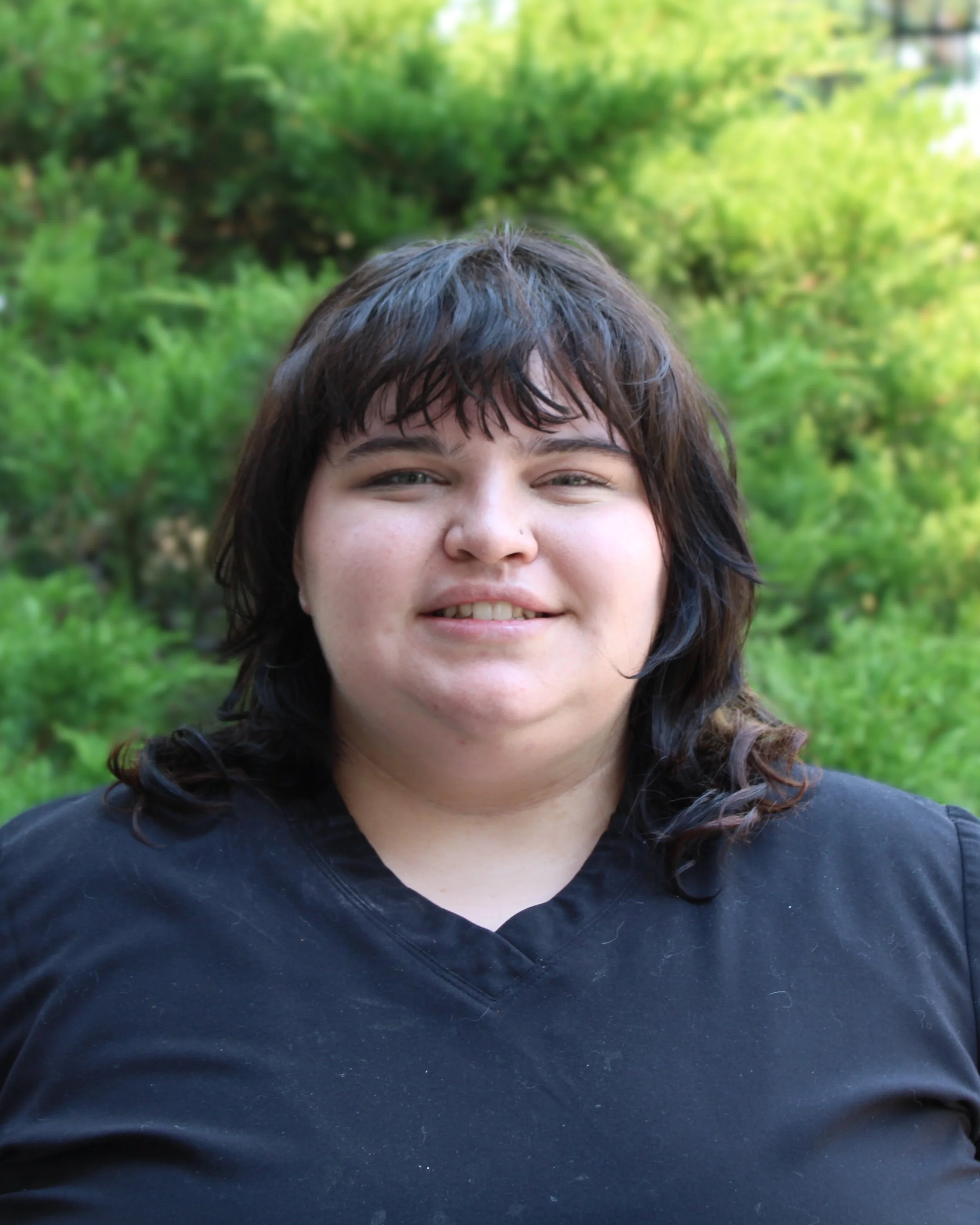 Woman with short dark hair, black scrubs, smiling