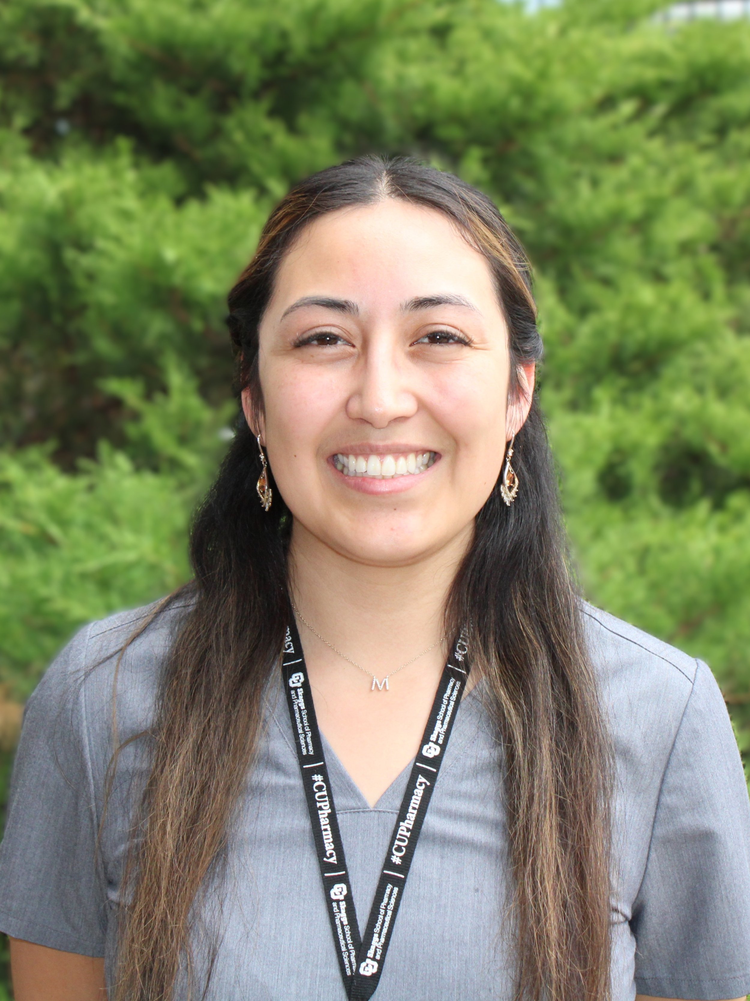 DIHFS Team - A smiling woman with long dark hair, wearing a grey scrub top, with a blurred background