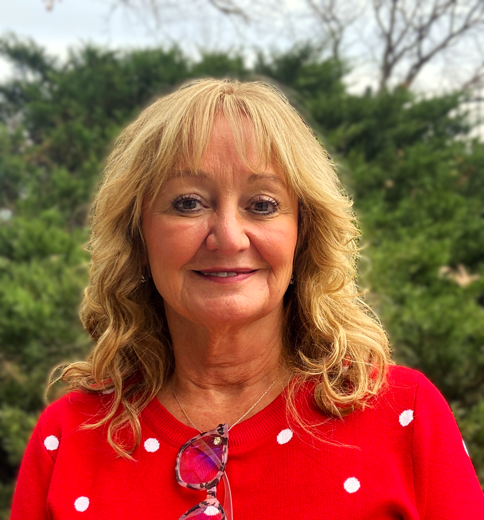 Woman with shoulder-length blond hair, wearing a red shirt with white dots, smiles at the camera. 
