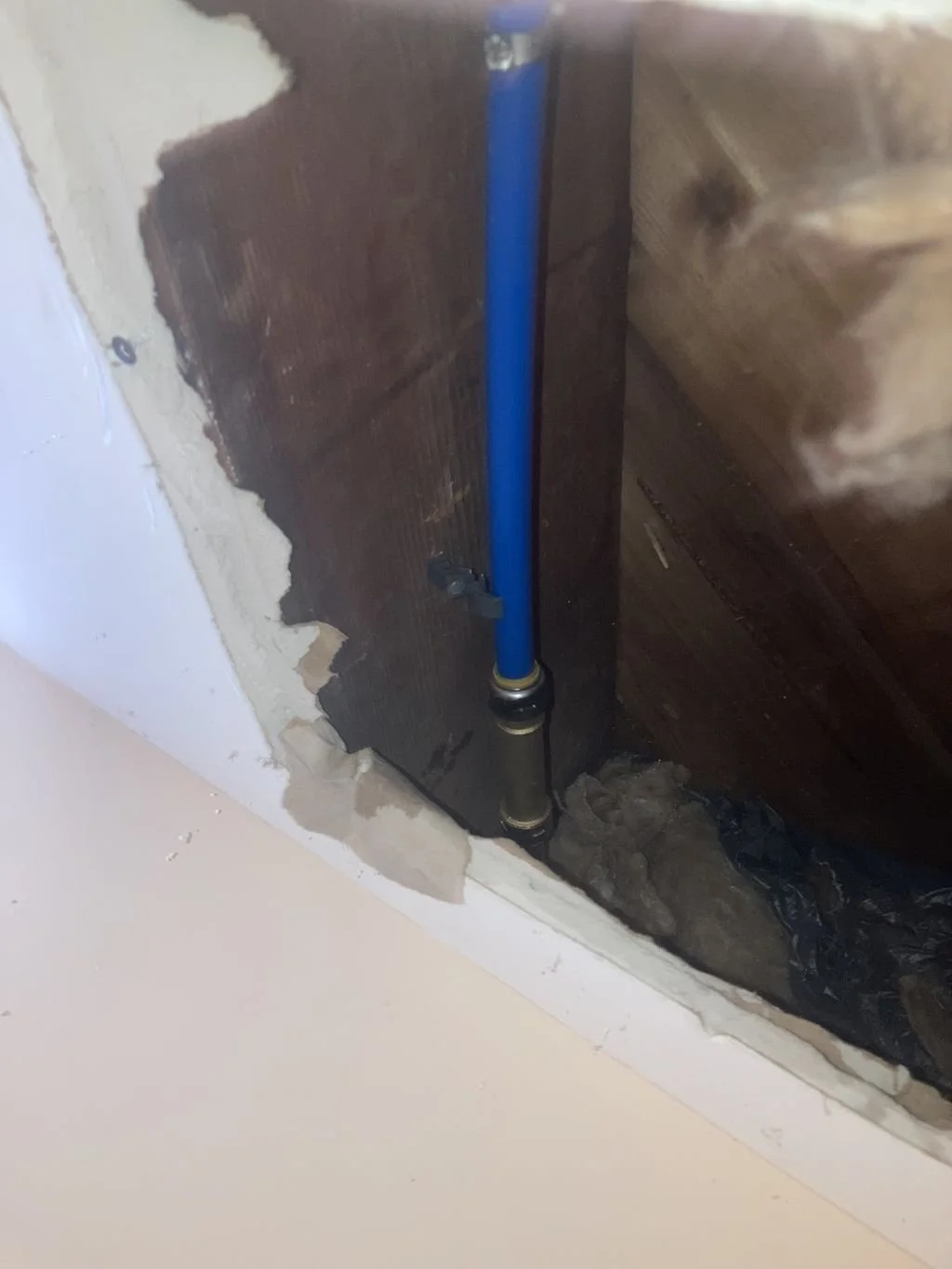 Close-up of a plumbing pipe running vertically in a wall opening under construction or renovation, with visible drywall and some debris.