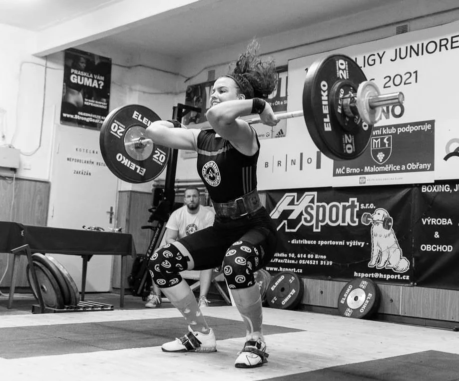 A woman lifting a barbell during a weightlifting competition in an indoor gym.