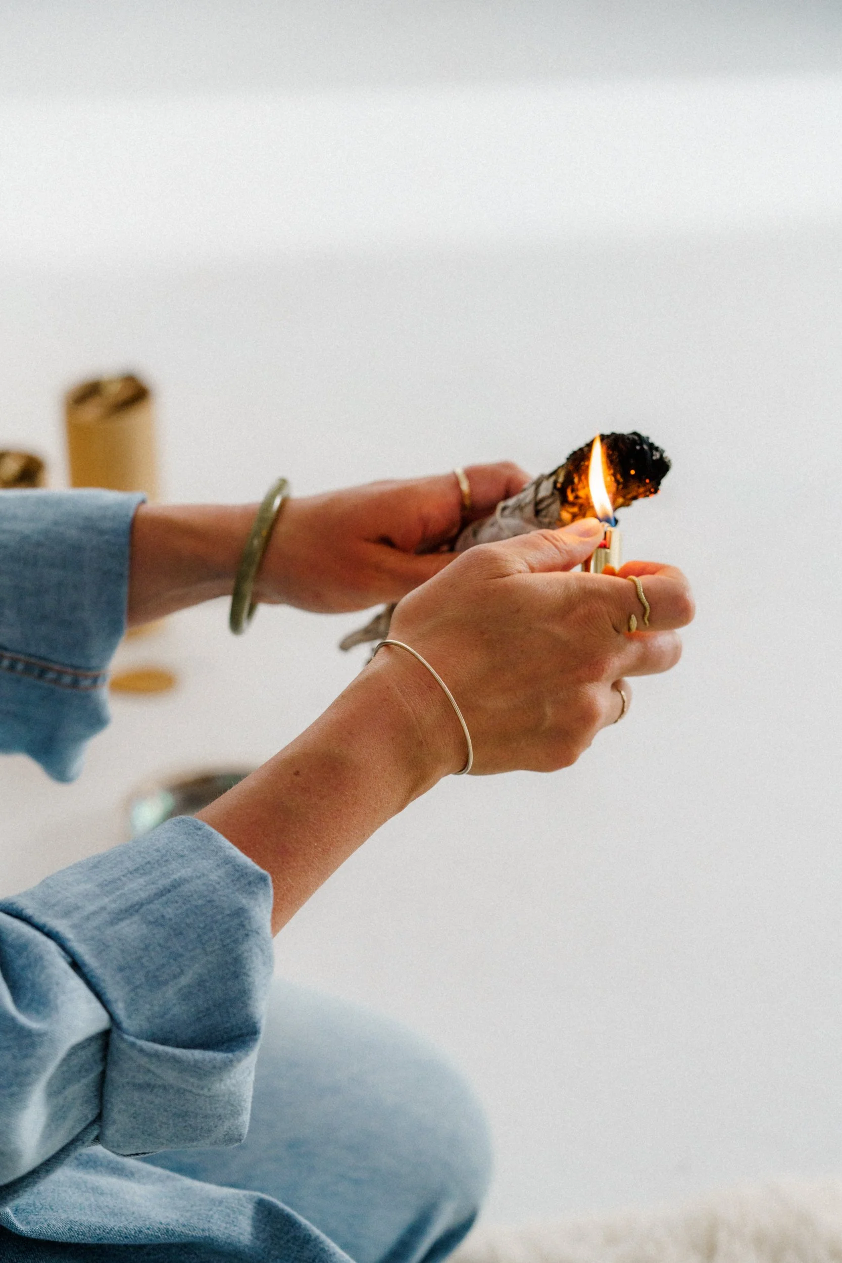 A person’s hands, wearing jewelry, burning sage.