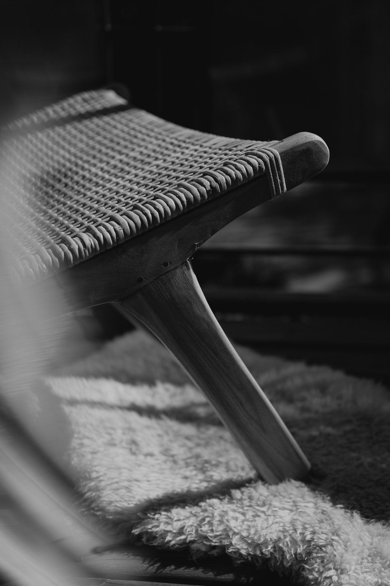 Black and white close-up of a modern woven lounge chair on a fluffy rug.