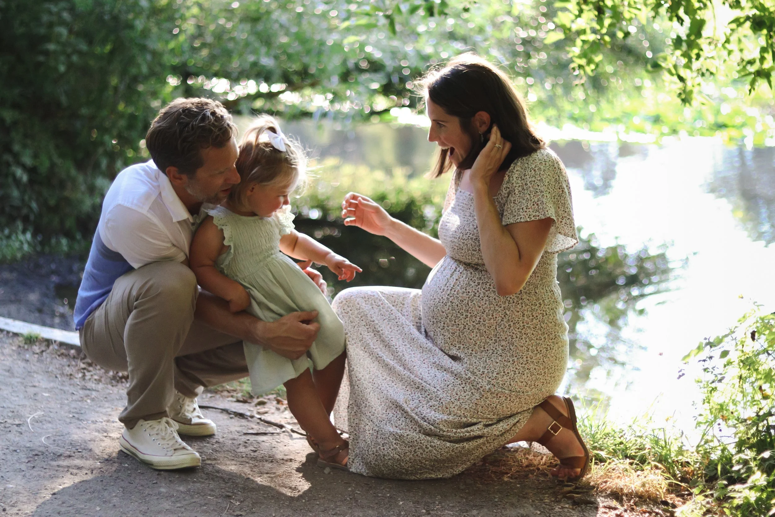 A family of three, including a father, a pregnant mother, and a young daughter, pose in the Seattle Arboretum for a family photoshoot.
