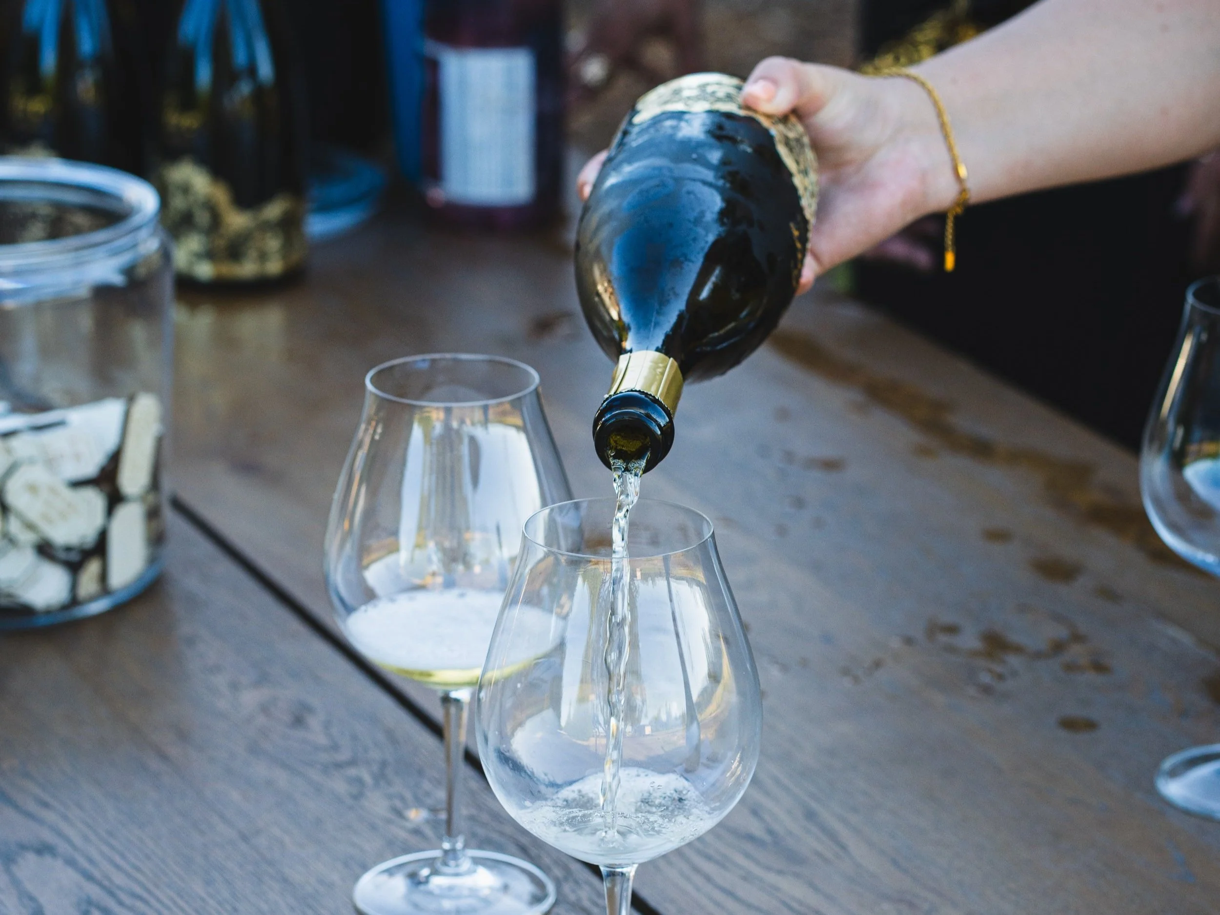 A person pouring champagne into wine glasses on a wooden table at an event in the Willamette Valley.